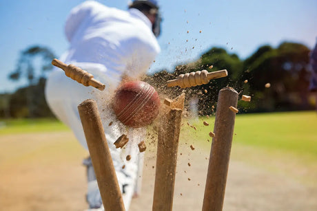 Cricket ball hitting the stumps with broken bails flying, highlighting common batting mistakes and the importance of proper cricket gear