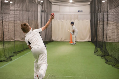 Junior cricketer bowling to a batter during indoor cricket practice in a net