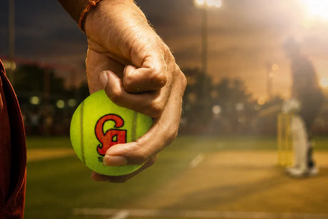 Close-up of a bowler gripping a bright green cricket tennis ball on a cricket pitch during an evening match