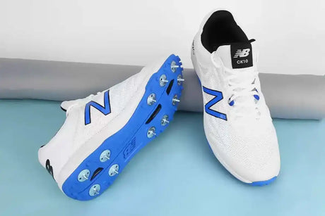 White and blue New Balance cricket shoes with metal spikes, designed for enhanced grip, stability, and performance for cricket players